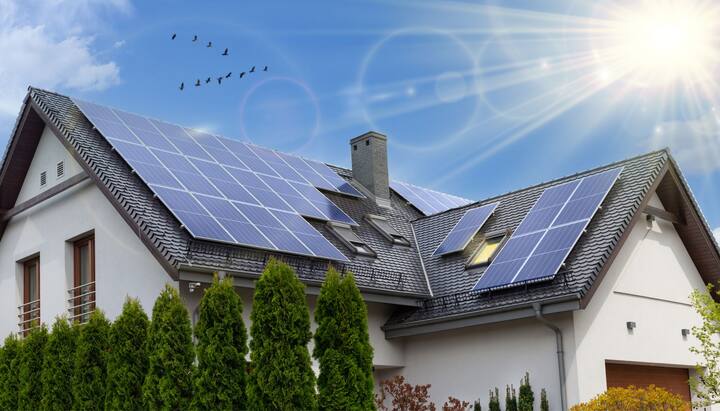 A close-up view of a residential rooftop solar panel installation in Staten Island, NY. The solar panels are arranged in a neat pattern and angled towards the sun to capture the maximum amount of energy. The roof of the house is visible in the background, with clear blue skies and a few clouds.